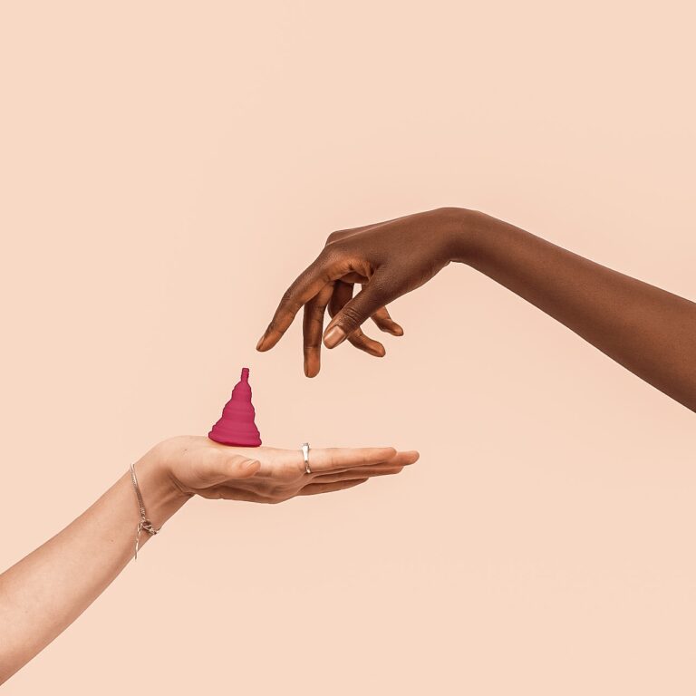a woman retrieving a pinkish purple menstrual cup from another woman's open hand
